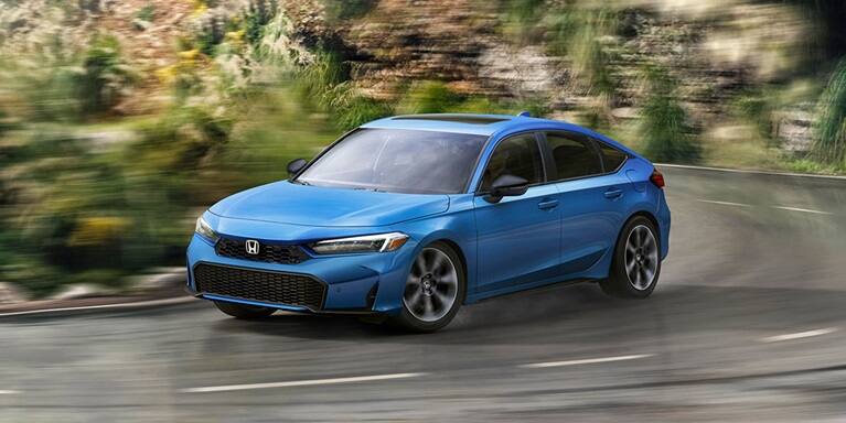 2026 Honda Civic Hatchback Sport Touring Hybrid in Boost Blue Pearl front driving on a winding road (Compact Hatchback).