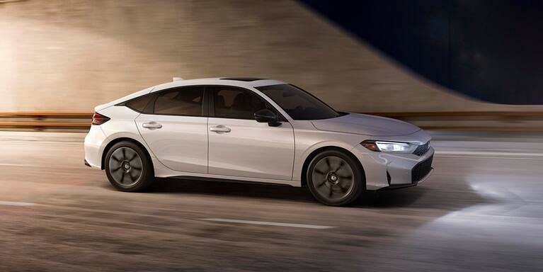 2026 Honda Civic Hatchback Touring Hybrid in Platinum White Pearl profile driving through a tunnel (Compact Hatchback).